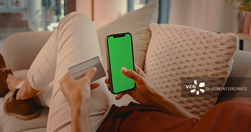 一名身份不明的人在家中使用手机并拿着信用卡图片素材