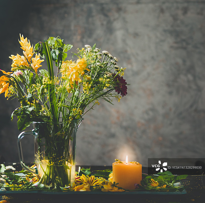 花园鲜花与黄色和紫色花朵，灰色墙壁背景下的黄色蜡烛图片素材