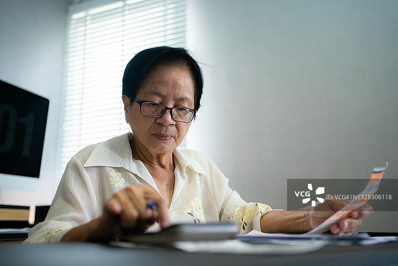 亚洲老年妇女计算每月开支并核对收据准备付款图片素材