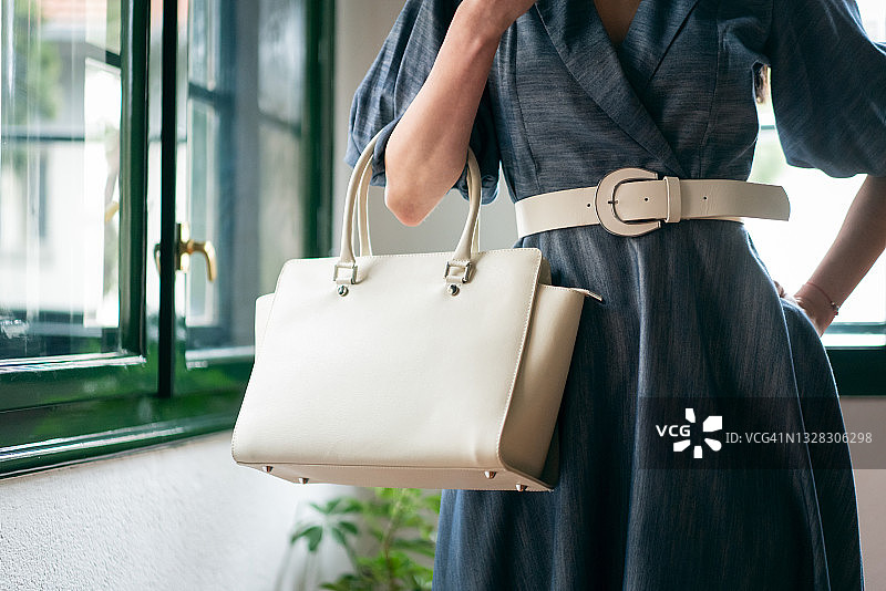 手提白色包包靠窗摆姿势的时装模特图片素材