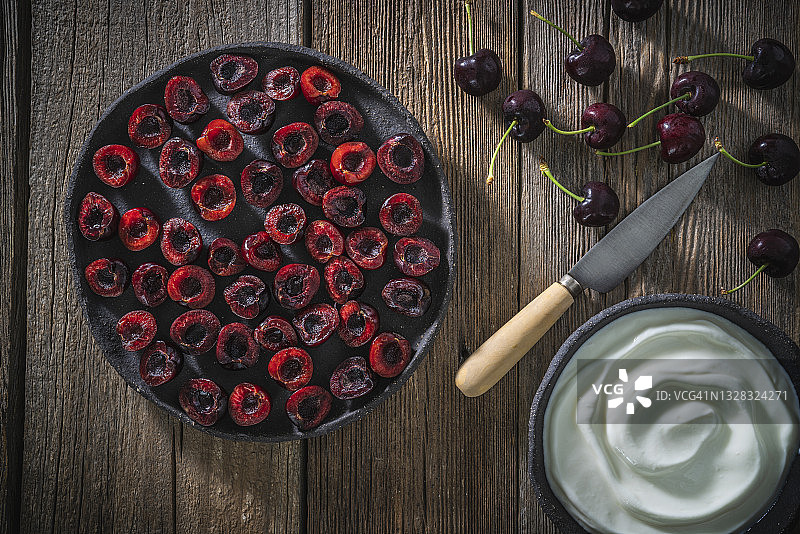 乡村木板上黑色盘子里的酸奶和半切新鲜樱桃图片素材