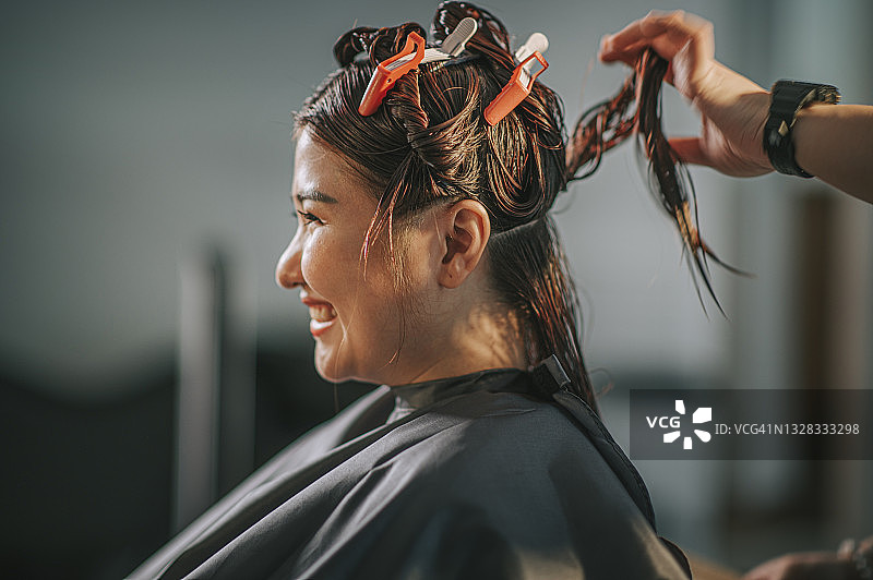 中国籍亚洲女发型师在美发沙龙为顾客梳理长发图片素材