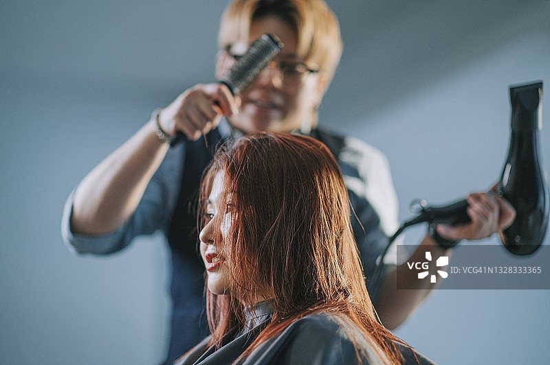 亚洲美发师在美发厅为顾客吹理湿长发图片素材