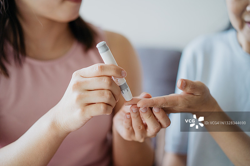 女性在家中帮助母亲用血糖仪检测血糖特写图片素材