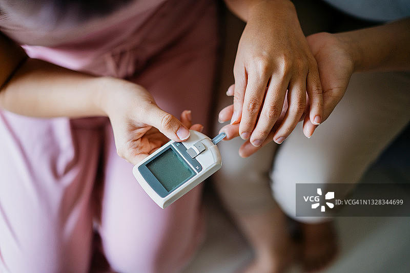 女性在家中帮助母亲用血糖仪检测血糖特写图片素材