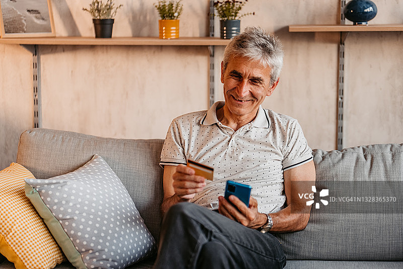 男人在沙发上用信用卡和手机购物图片素材