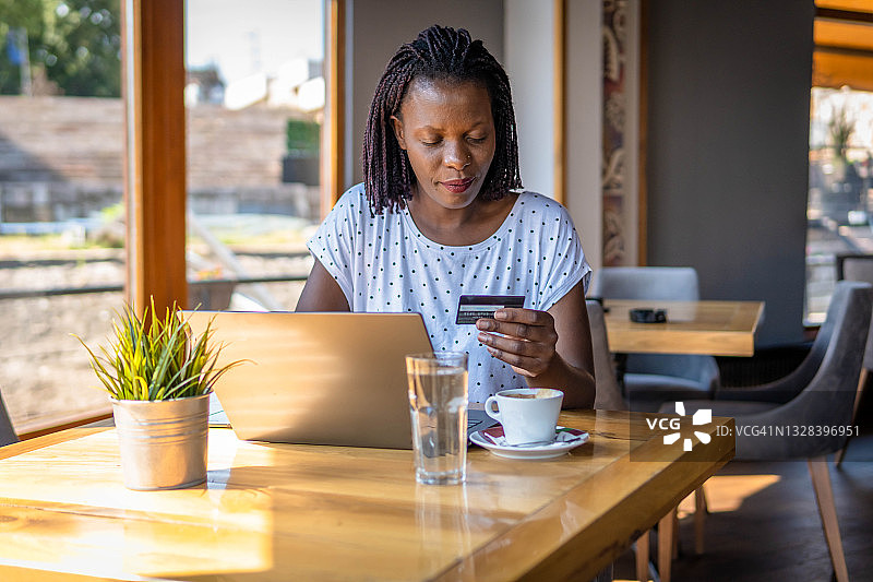 年轻的非裔美国女性在咖啡馆使用笔记本电脑和信用卡进行网上购物图片素材