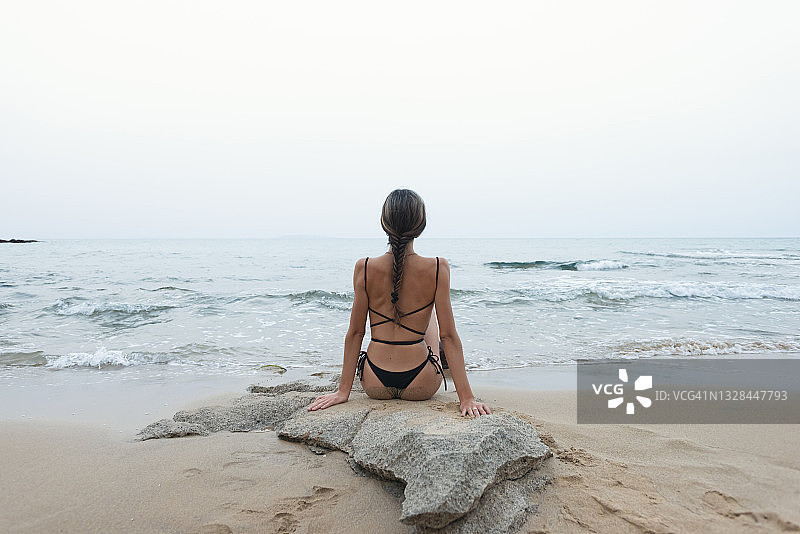 穿着比基尼，梳着辫子坐在海边的女人图片素材