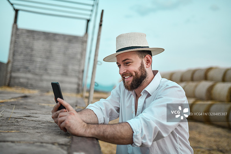 微笑的现代农民在田野里使用智能手机图片素材