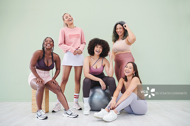 一群穿着健身服的女性在绿色背景前摆姿势的全身照图片素材