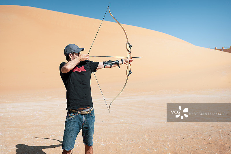 男子在沙漠中练习射箭，瞄准靶心图片素材