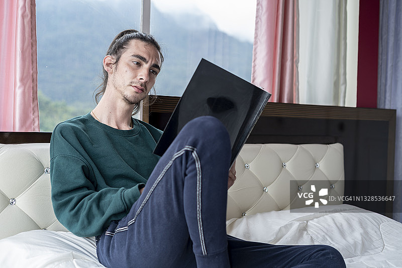 拉丁裔男子坐在床上看书图片素材