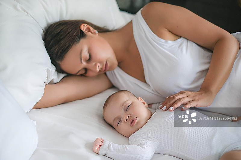 睡在新生儿旁边的疲惫的新手妈妈图片素材