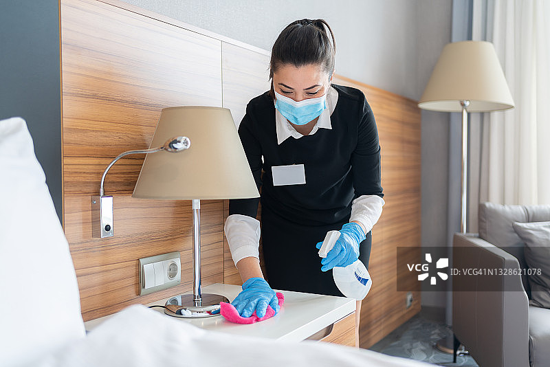 家政人员在酒店房间内戴防护口罩用消毒喷雾清洁家具图片素材