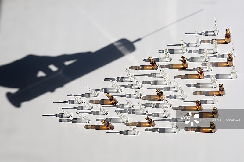 大量玻璃安瓿瓶前的可重复使用的大型旧注射器轮廓图片素材