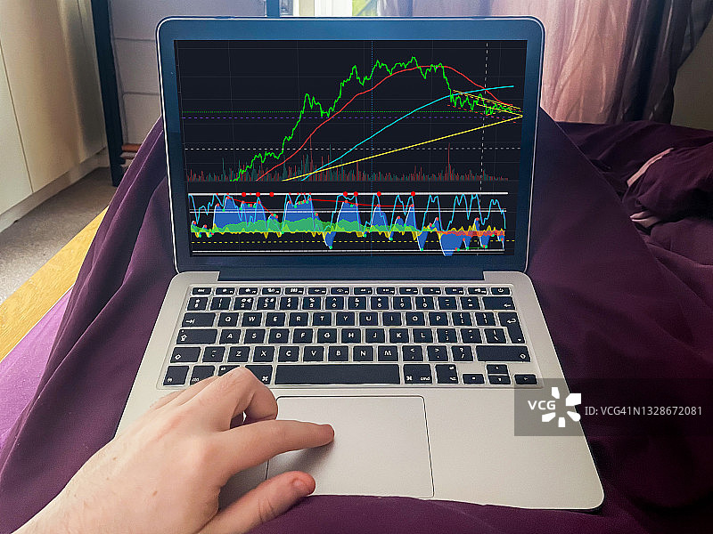 男人在床上用笔记本电脑工作，在家交易股票和加密货币图片素材