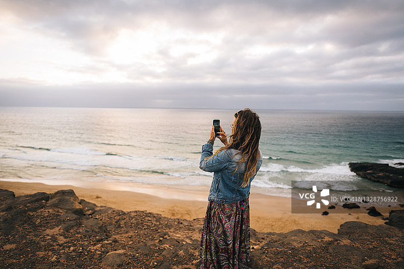 年轻女人用手机在海岸悬崖上拍照图片素材