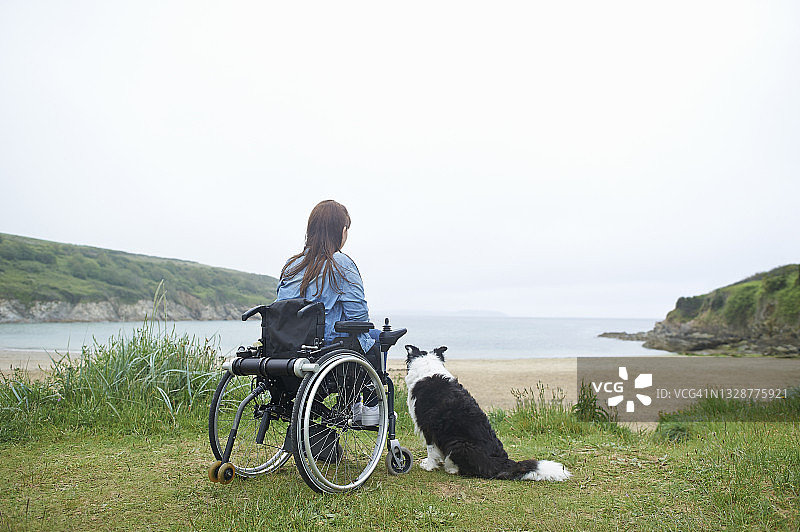 坐在轮椅上，带着狗在海滩边看海的女人图片素材