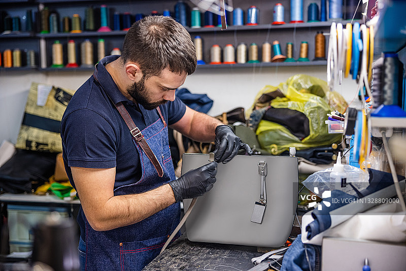 在工艺品修理店里，年轻男子正将带子穿过女式钱包上的扣环图片素材