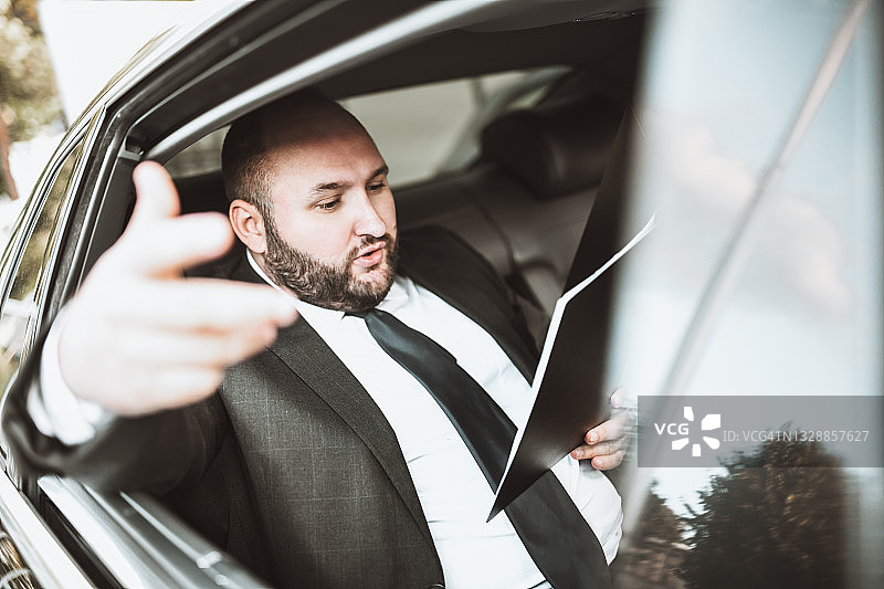 旅行中，表情严肃的光头商人正在用写字板思考公司生产数据图片素材