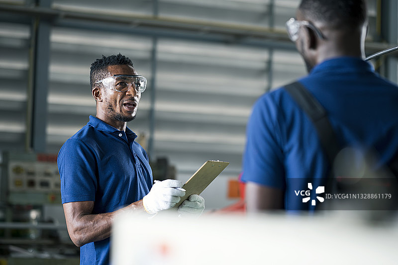 工厂工人在铣床前讨论汽车零件的生产计划图片素材