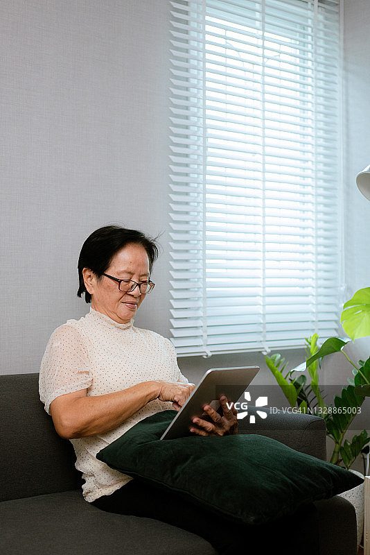 在客厅使用平板电脑的亚洲老年妇女图片素材