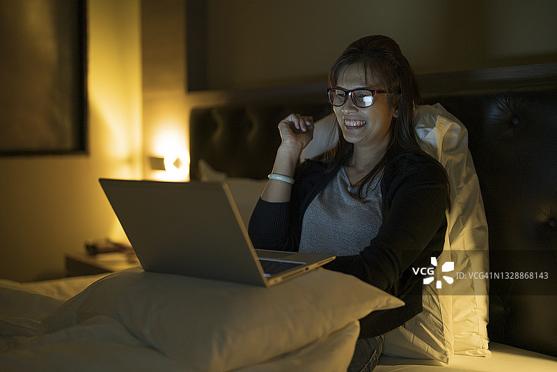 年轻女人晚上在床上用笔记本电脑看电视。图片素材
