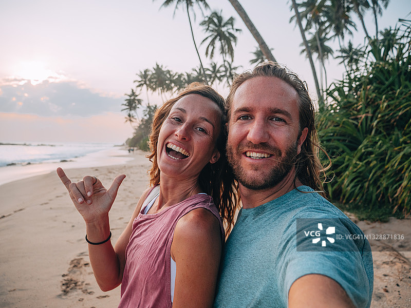 年轻情侣在热带海滩日落时用手机自拍图片素材