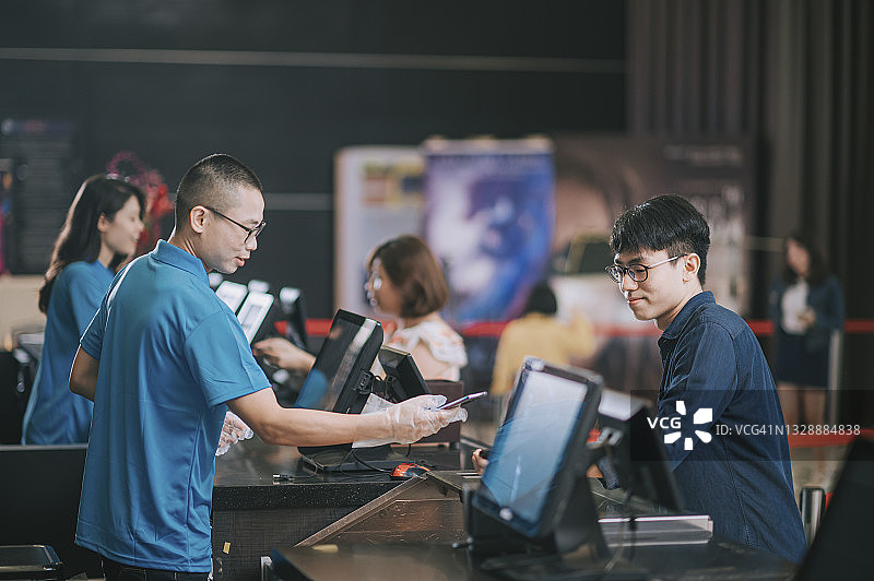 在电影院吧台点餐的亚洲青年男人，购买爆米花和矿泉水等待电影开场图片素材