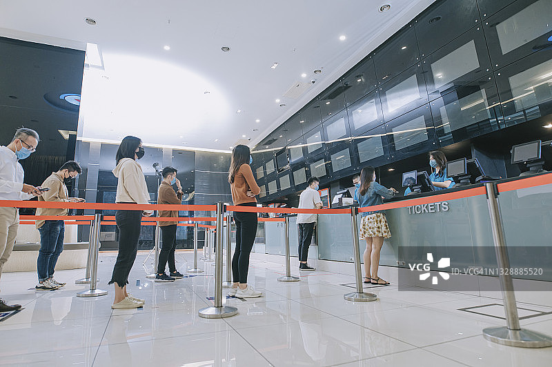 在电影院售票柜台前排队等候的亚洲观众购买电影票、爆米花和饮料，电影放映前使用非接触式支付图片素材