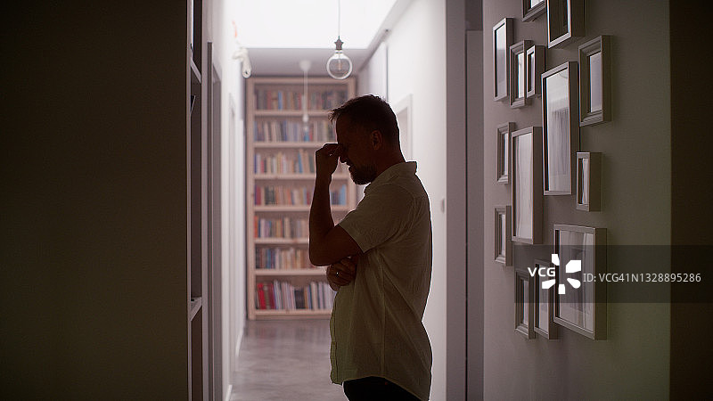 男子在家中幽闭黑暗的走廊里感到不适，双手抱头靠墙图片素材