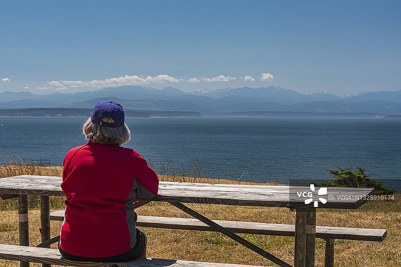 坐在桌旁看着普吉特海湾的穿红色外套的年长女性图片素材