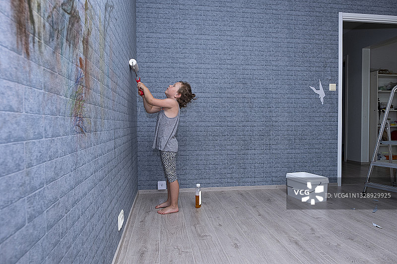 6岁高加索女孩在墙上绘画，手持油漆滚筒图片素材
