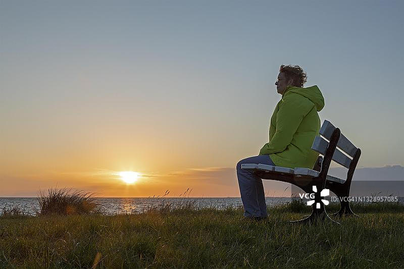 在德国格罗森布罗德西海滩的长椅上欣赏日落的女人图片素材