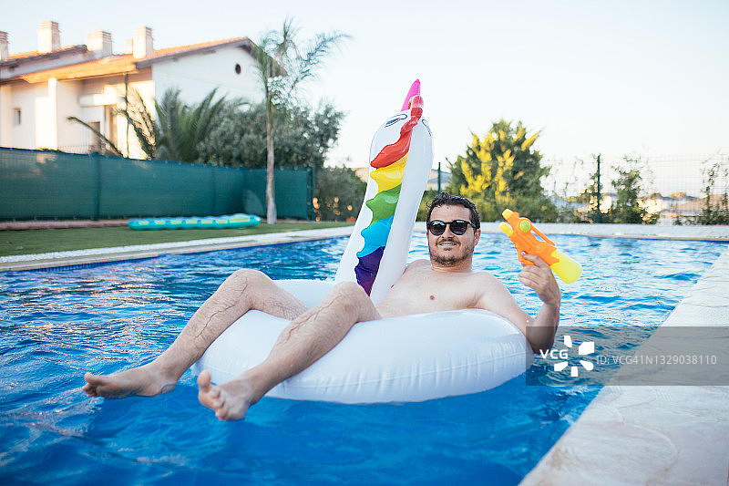 男子在游泳池里骑着独角兽，拿着水枪图片素材