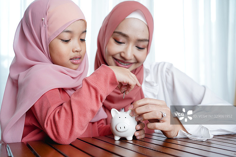 亚洲穆斯林家庭将硬币放入白色储蓄罐。收入、储蓄和金融概念。图片素材