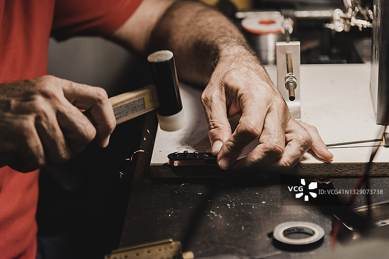工匠用锤子将圆柱形磁铁插入吉他拾音器图片素材
