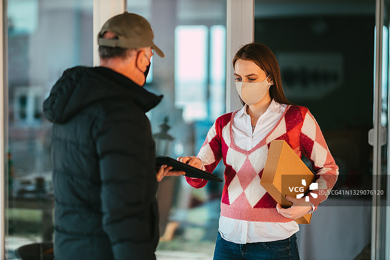 戴口罩的女人从邮递员那里收到包裹图片素材