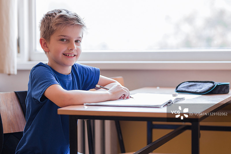 坐在书桌前微笑的可爱男学生图片素材