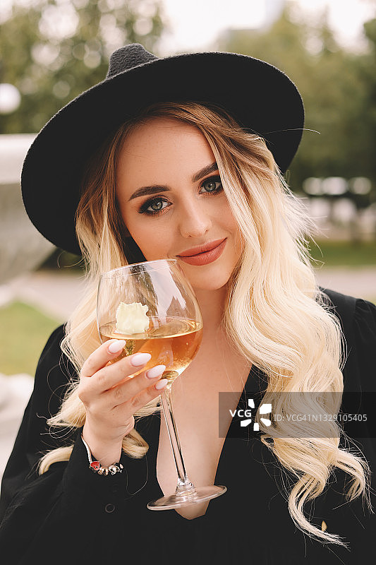 优雅的金发女子在公园剧院旁品酒图片素材