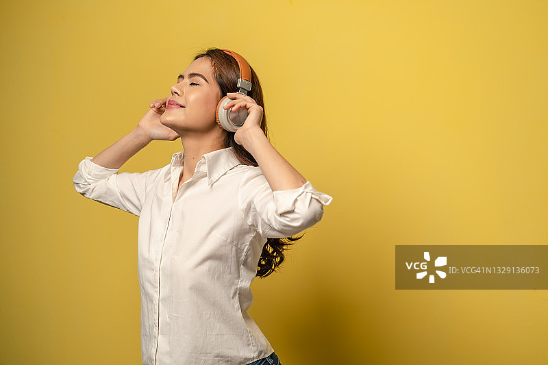 年轻漂亮的女人在黄色背景上用无线耳机听音乐图片素材