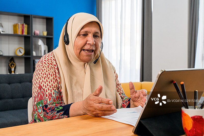 戴着头巾和耳机的穆斯林妇女在笔记本电脑上观看网络研讨会图片素材