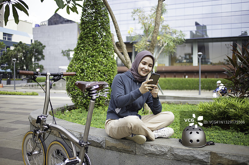 骑自行车后的亚洲年轻戴头巾女子正在使用智能手机图片素材