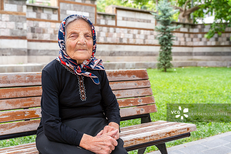 年长的女人坐在长椅上，对着镜头微笑图片素材
