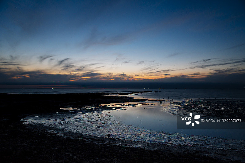 日落时分岩石海岸线上平静水面上的壮丽云彩图片素材