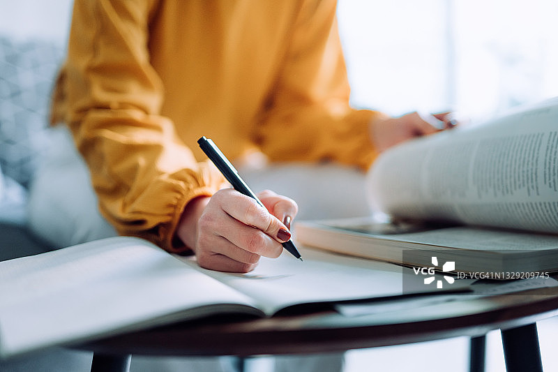 特写：年轻亚洲女性在家中专注读书并做笔记，专注于学业图片素材