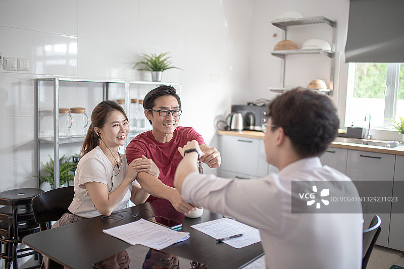 亚洲华人夫妇在厨房与保险代理人握手洽谈保险事宜图片素材