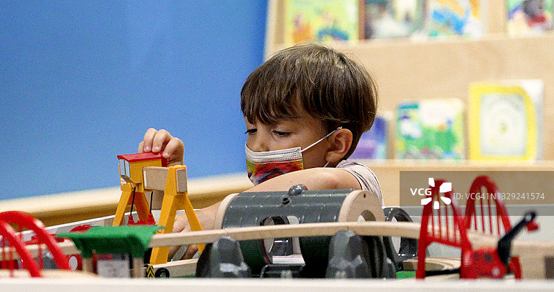戴着防护口罩的小男孩在幼儿园教室里玩耍图片素材