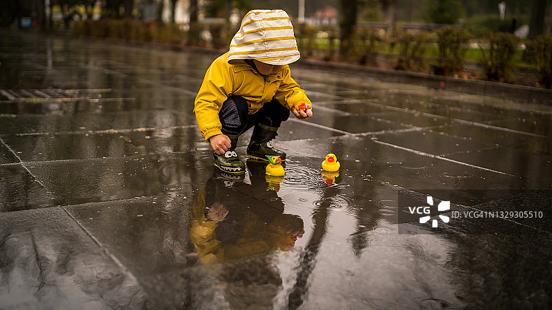 可爱的宝宝穿着黄色雨衣和雨靴在雨天玩鸭子图片素材