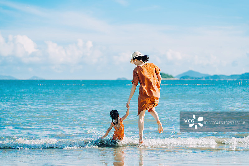 阳光明媚的夏日，快乐的亚洲母女手牵手在海滩上跳跃图片素材